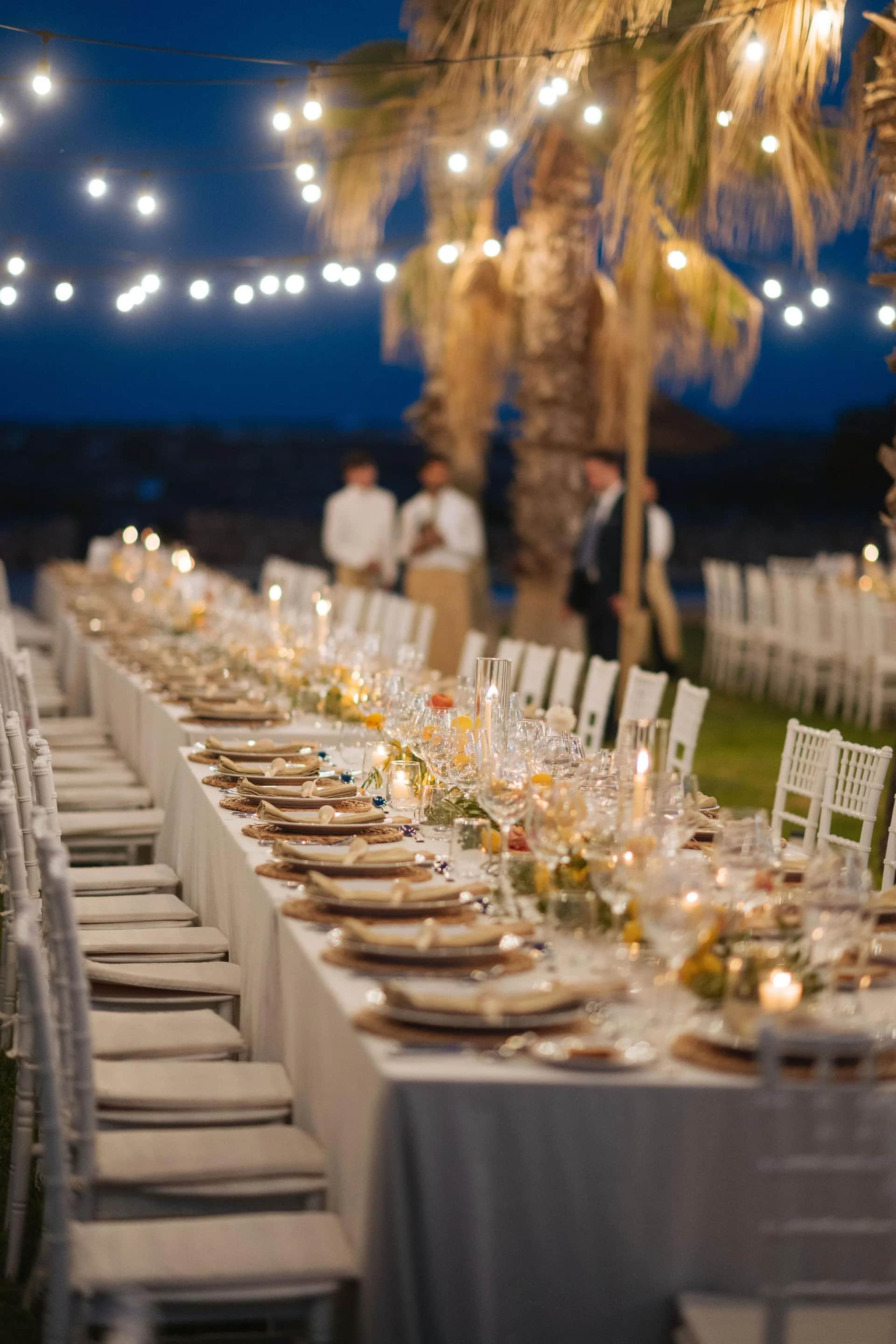 Longue tablée de mariage à l'heure bleue, chaises chiavari et guirlandes guinguette sous les palmiers