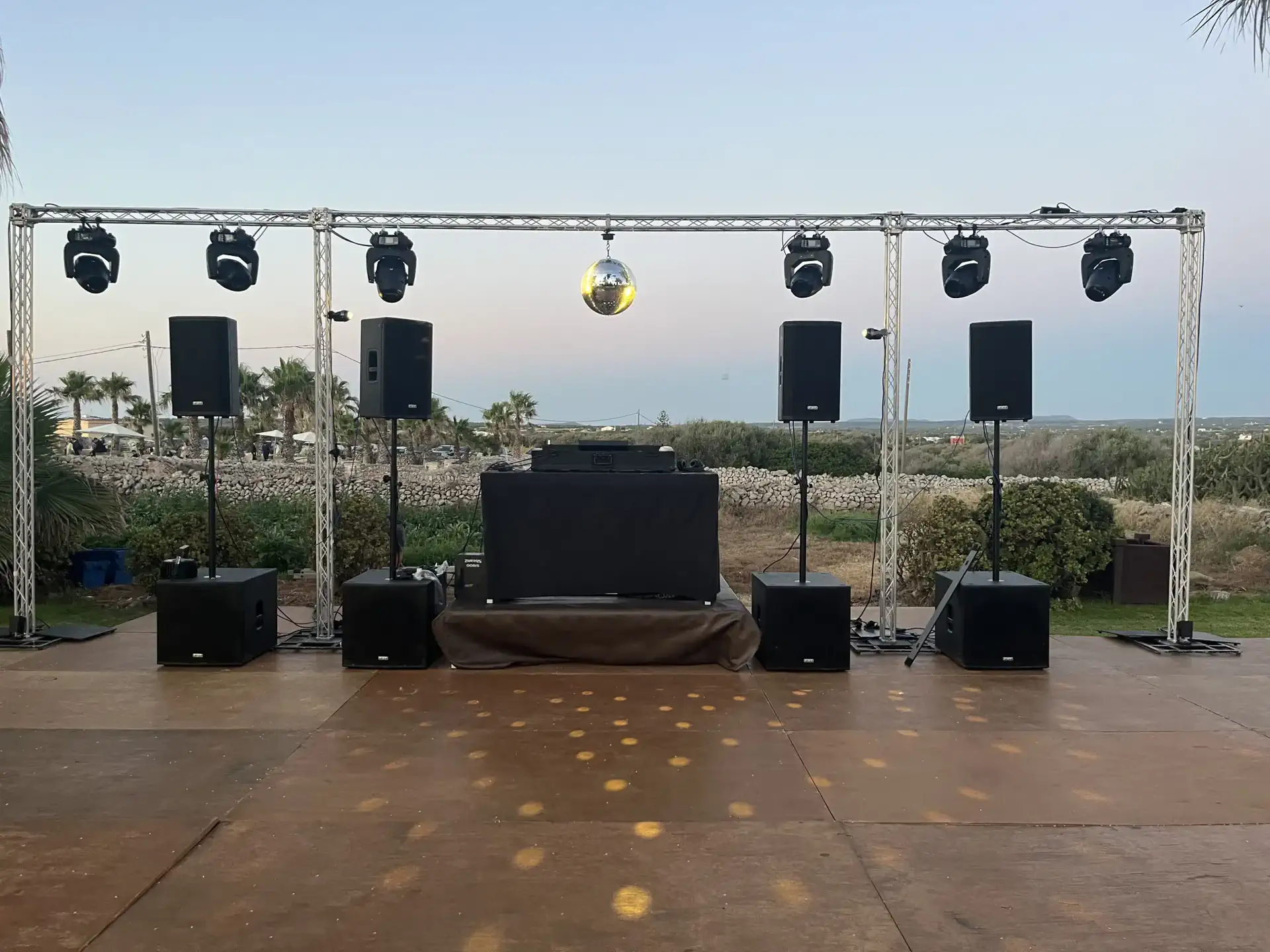 Scène DJ en extérieur avec enceintes, caissons de basse et lyres sur structure