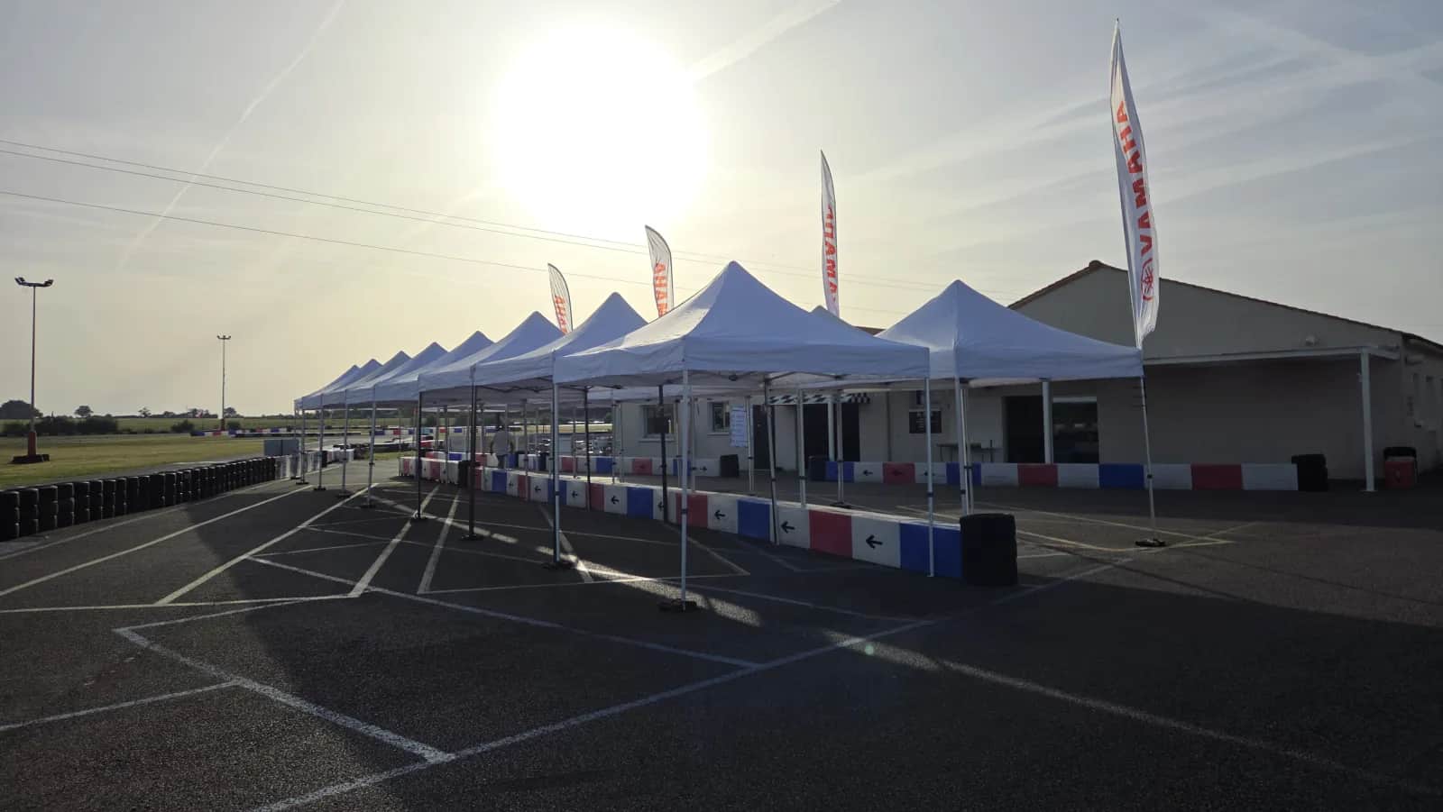 Row of pop-up gazebos backlit at sunrise on the Mécamax circuit, Yamaha flags