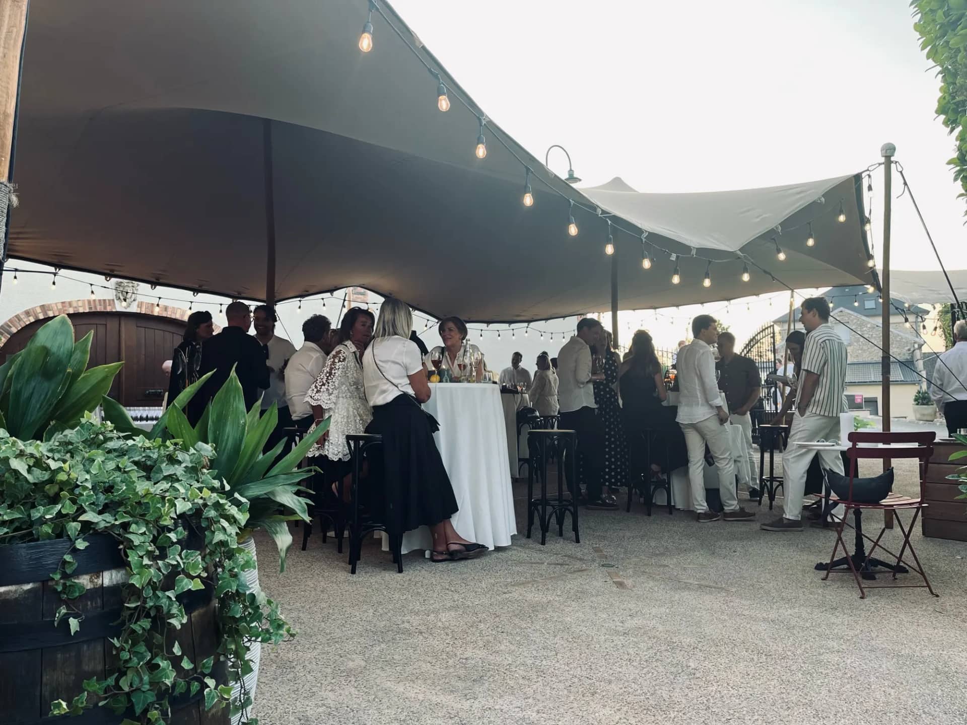 Cocktail under an ecru stretch tent on wooden poles in Mutigny, festoon lights and white-draped high tables