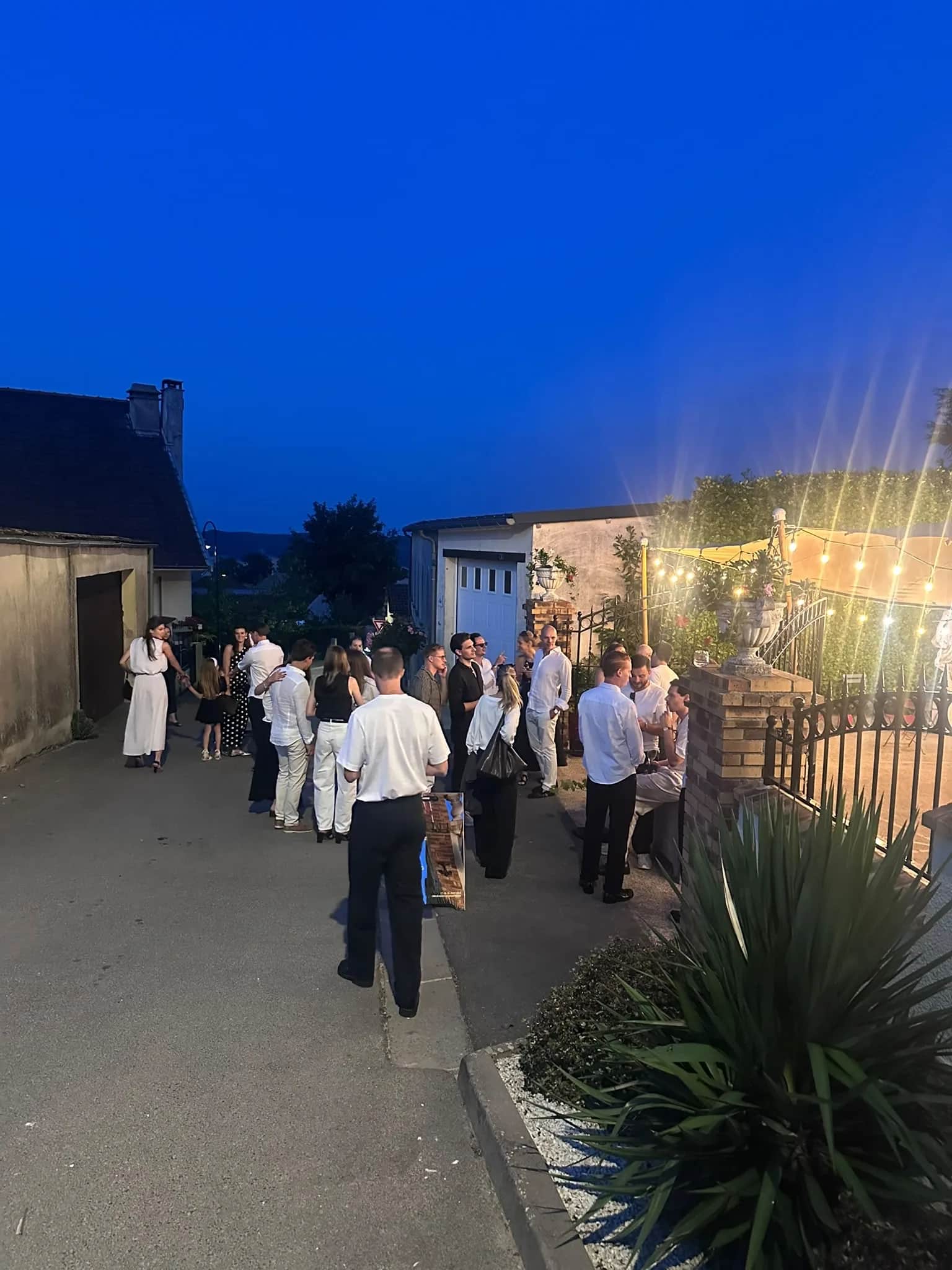 Evening under a stretch tent at dusk in Mutigny, festoon lighting and guests on a paved courtyard in front of stone buildings