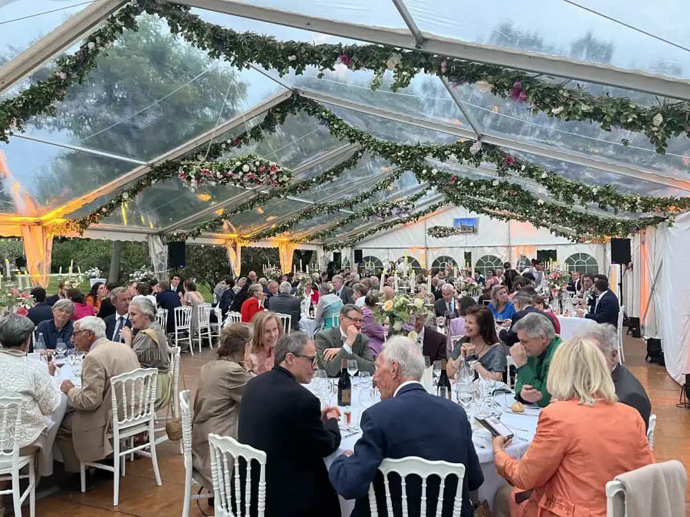Evening wedding reception under a crystal-clear pitched-roof tent open onto the grounds with mood lighting