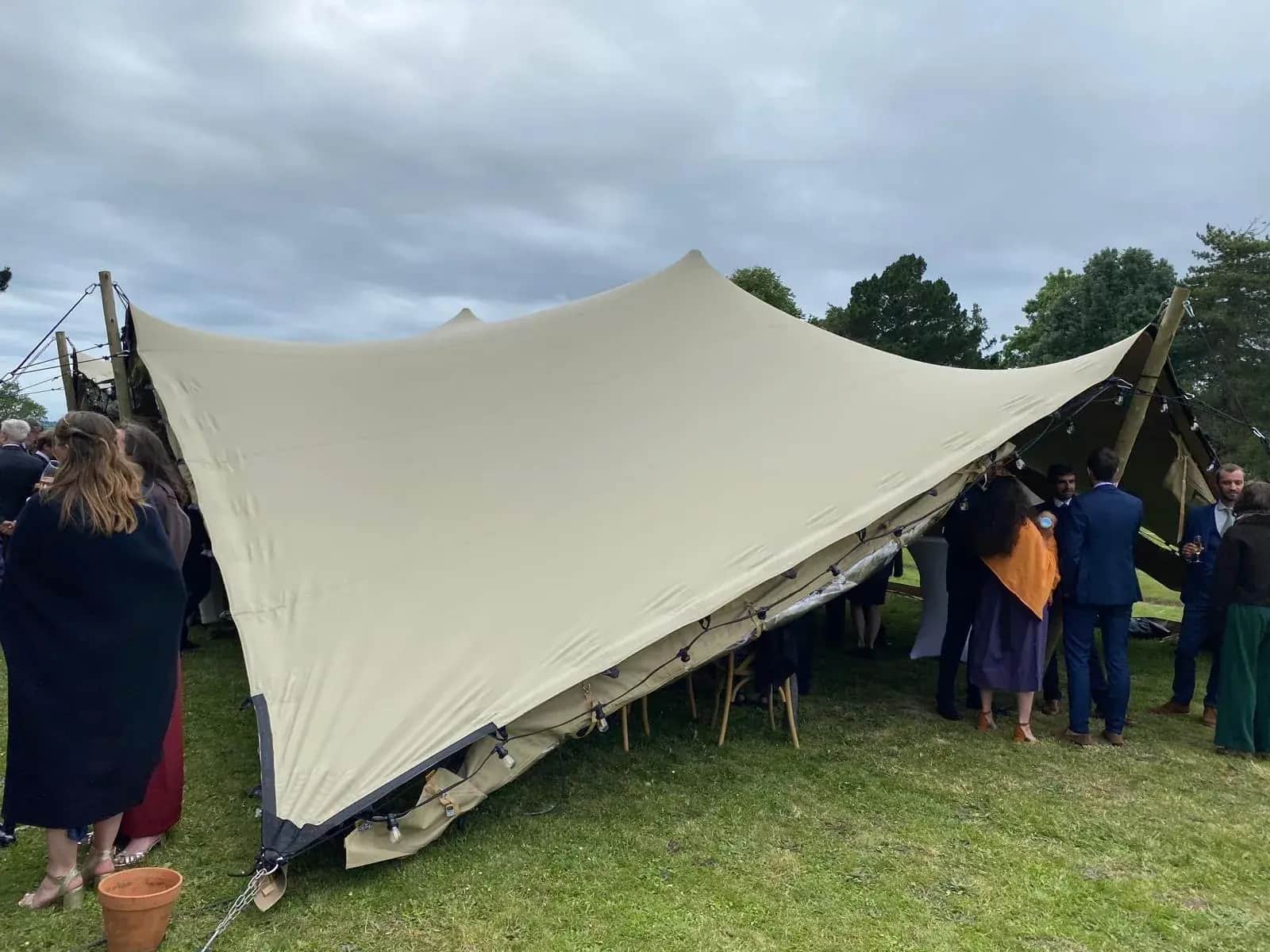 Ecru stretch tent on wooden poles with festoon lighting for an outdoor wedding cocktail