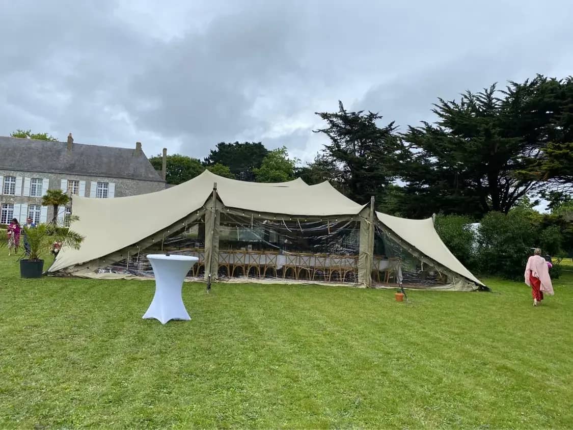 Ecru stretch tent closed with crystal-clear sidewalls, set up in front of a château for a wedding dinner