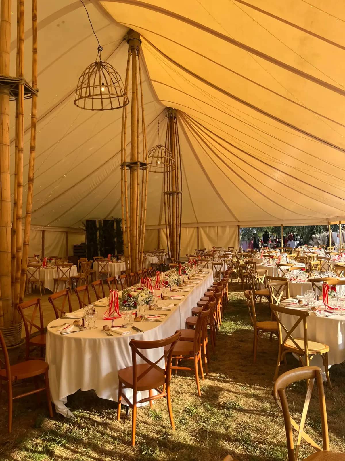 Long white wedding banquet table under the bamboo marquee, wooden bistro chairs, bamboo poles and cage pendant lights