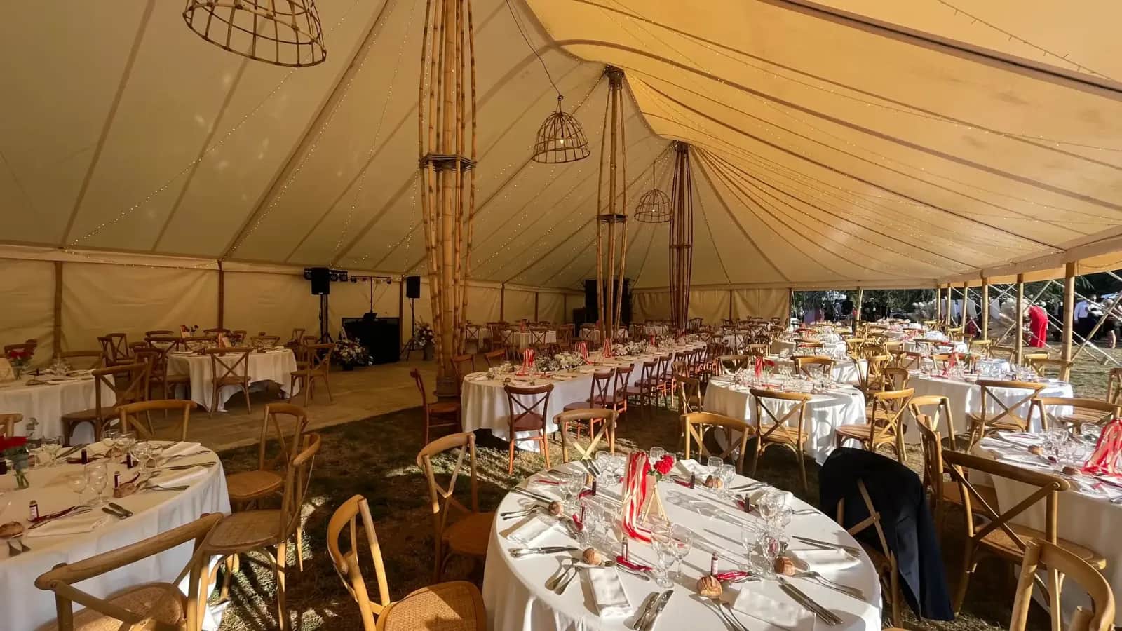Interior of the bamboo marquee: bamboo poles, bamboo cage pendant lights and round tables dressed in white with wooden bistro chairs, château grounds in the background